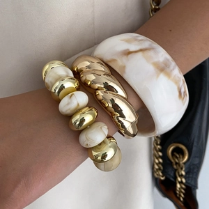 Stacked vintage resin and gold chain bracelets with marble textures on model's wrist