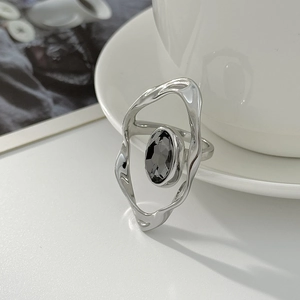 Detail of irregular silver ring with oval dark gemstone on a minimalist white desk