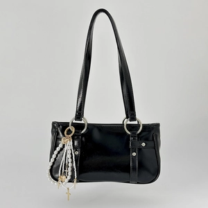 Detail of glossy black shoulder bag featuring pearl chains with cross and heart charms