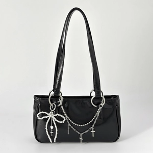 Detail of silver cross pendants and white pearl bow charm on a black glossy handbag