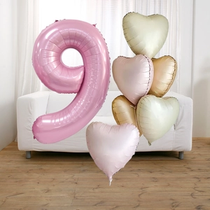 Detail of pink number 9 and macaron heart balloons set against a white sofa background