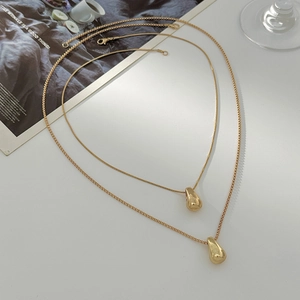Vue rapprochée de colliers dorés avec pendentifs gouttes polies sur fond blanc pur