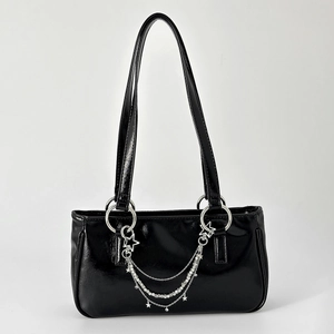 Detail of glossy black leather bag featuring silver multi-layer chains and star charms