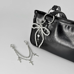 Bow pearl bag charm and double layered silver cross keychain on black tote bag