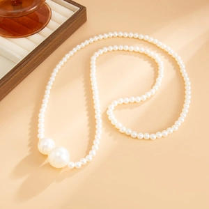 Detail of beaded pearl necklace with two large accent pearls on a minimalist background