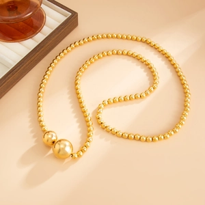 Macro detail of a layered gold beaded necklace with two polished solid metal spheres