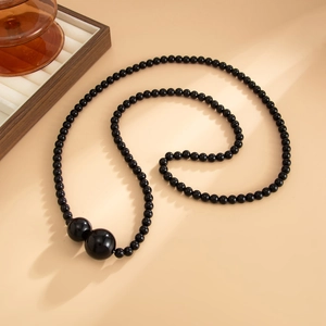Close-up of black beaded necklace with large polished accent pearls on a beige surface