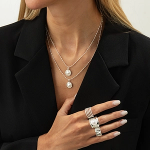Silver jewelry set with layered pearl necklace and textured rings on black blazer