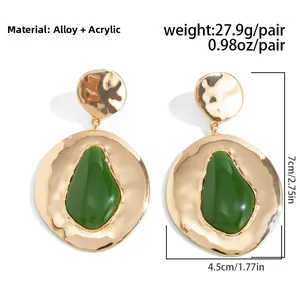 Detail van grote gouden gehamerde oorbellen met groene peervormige stenen en metaal