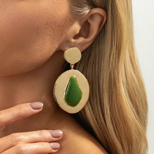 Close-up van model met grote goudkleurige druppeloorbellen met groene accenten