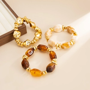 Detail of stacked bohemian bracelets with gold beads, marble resin, and amber tones