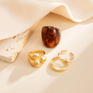 Detail of amber resin ring and gold metal rings set on beige stone and silk fabric