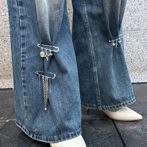 Close-up of a silver pin with stars, heart charms and long chain tassels on blue jeans