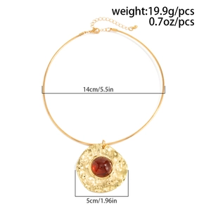 Detail of gold metal choker necklace with red resin gemstone and hammered pendant texture