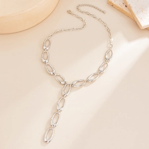 Close-up of a silver Y-shaped tassel necklace with wide oval links on a stone texture