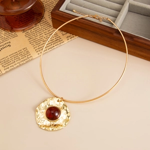 Detailed close-up of golden hammered metal choker with central resin gemstone pendant