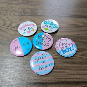 Close-up of Gender Reveal tinplate badges with Mommy and Daddy to be motifs on wood