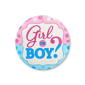 Close-up of a tinplate gender reveal badge with pink and blue Girl OR BOY? design