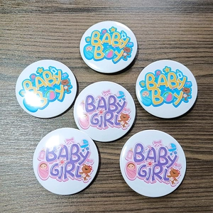 Tinplate baby shower badges with Baby Boy and Baby Girl cartoon designs on wood background