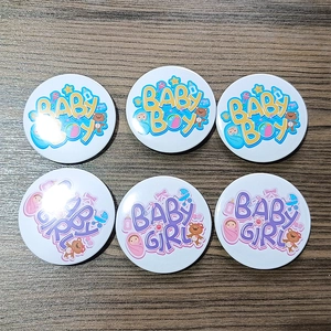 Detailed view of 6-piece baby shower tinplate badges for gender reveal on wood surface