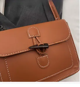Detail of vintage brown leather crossbody bag with toggle closure and white stitching