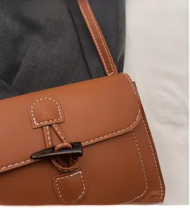 Detailed close-up of brown leather crossbody bag featuring toggle closure and contrast stitching