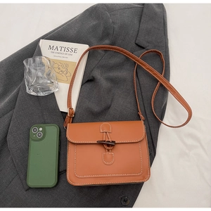 Detail of a brown leather crossbody bag with white stitching and wood toggle closure