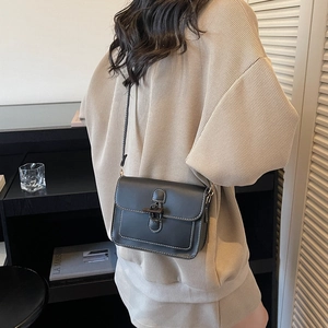 Chic black crossbody bag with white stitching and retro metal buckle on a model