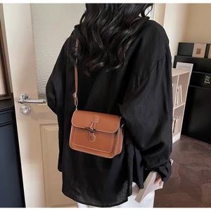 Brown leather crossbody bag with white stitching and horn buckle closure in retro style