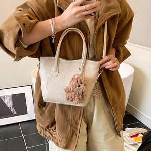 Borsa a secchiello beige minimalista con tracolla e ciondolo a forma di orsetto