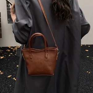 Dettaglio di una borsa a secchiello in pelle PU marrone con tracolla e logo inciso