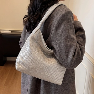 Sac hobo tressé argenté porté à l'épaule par un mannequin en manteau gris élégant