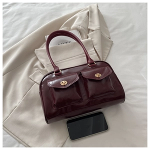Detail view of burgundy leather handbag with gold twist-locks on white bedding background