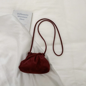 Detail of burgundy suede dumpling bag with pleated drawstring and thin crossbody strap