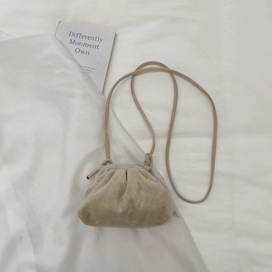 Close-up of beige ruched cloud bag with fine shoulder strap on white fabric texture