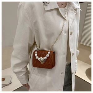Detail of brown woven mini bag with pearl handle and golden heart clasp on model