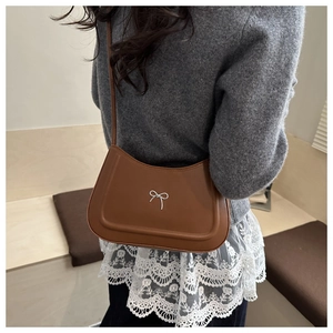 Brown leather underarm bag with silver bow detail worn by a model to show size