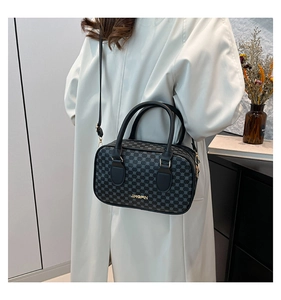 Détail du sac Boston noir avec ferrures dorées porté par un mannequin en manteau blanc