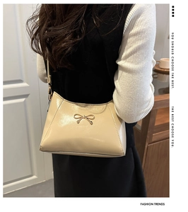 Close-up of beige patent leather crescent bag with golden bow metallic hardware