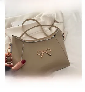Detailed view of beige crossbody bag with golden metal bow buckle and textured leather