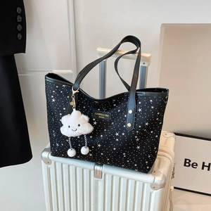 Black star print tote bag with plush cloud charm on a white suitcase for stylish travel