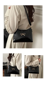 Detail of glossy black shoulder bag with a sleek golden bow buckle on the strap