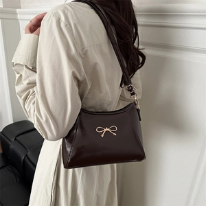 Dark brown patent leather shoulder bag with gold bow accent worn by a model