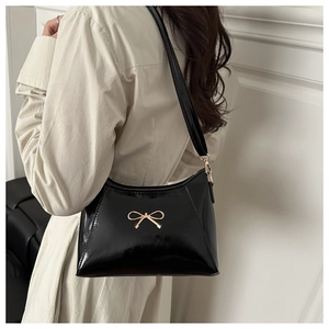 Detail of black glossy shoulder bag with a decorative gold metal bow buckle and strap