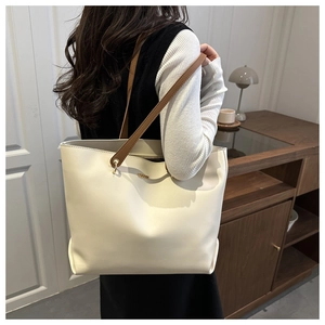Detail view of a large cream tote bag with brown straps in a cozy home setting
