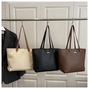 Three minimalist leather tote bags in cream, black, and brown hanging on display racks