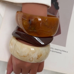 Three wide marble pattern resin bangles in amber, coffee and cream on a fashion book