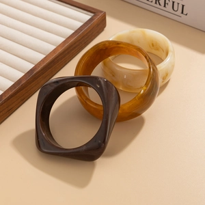 Detail shot of three resin bangles in amber tortoise and marble patterns on warm surface
