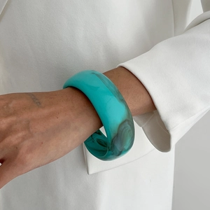 Détail d'un bracelet en résine turquoise à effet marbré porté sur un costume blanc