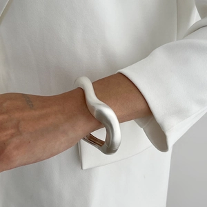 Détail du bracelet argenté mat ondulé avec une large silhouette fluide et finition métal